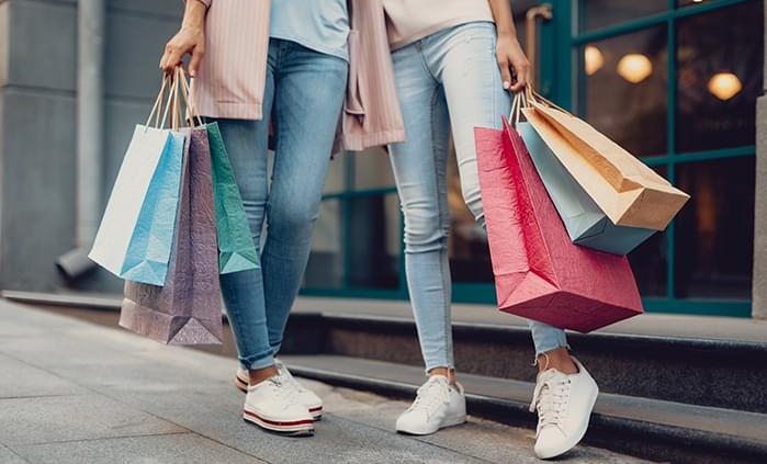2 women are stepping out of a retail outlet holding their shopping bags