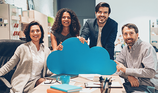A smiling group at a desk holds onto a large cloud cutout illustrating cloud services